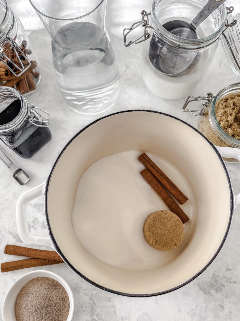 Cinnamon simple syrup dry ingredients (granulated sugar, brown sugar, and cinnamon sticks) in a white cast iron pot.