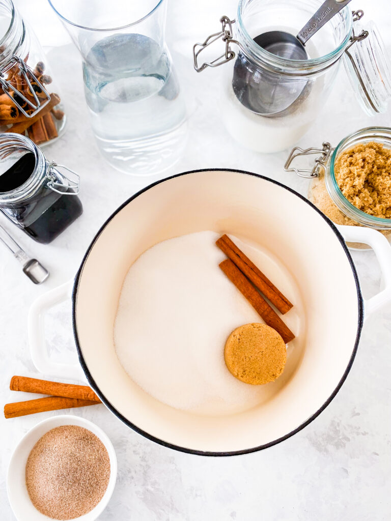 Cinnamon simple syrup dry ingredients (granulated sugar, brown sugar, and cinnamon sticks) in a white cast iron pot.