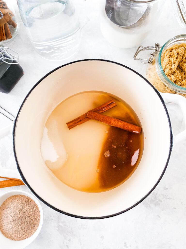 Cinnamon simple syrup ingredients (water, granulated sugar, brown sugar, cinnamon sticks, and vanilla) in a white cast iron pot.