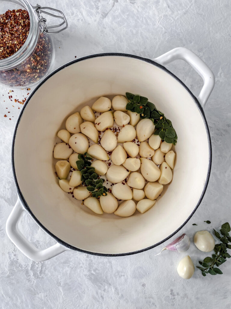 Garlic, oregano, and red pepper flakes in a white cast-iron pot.