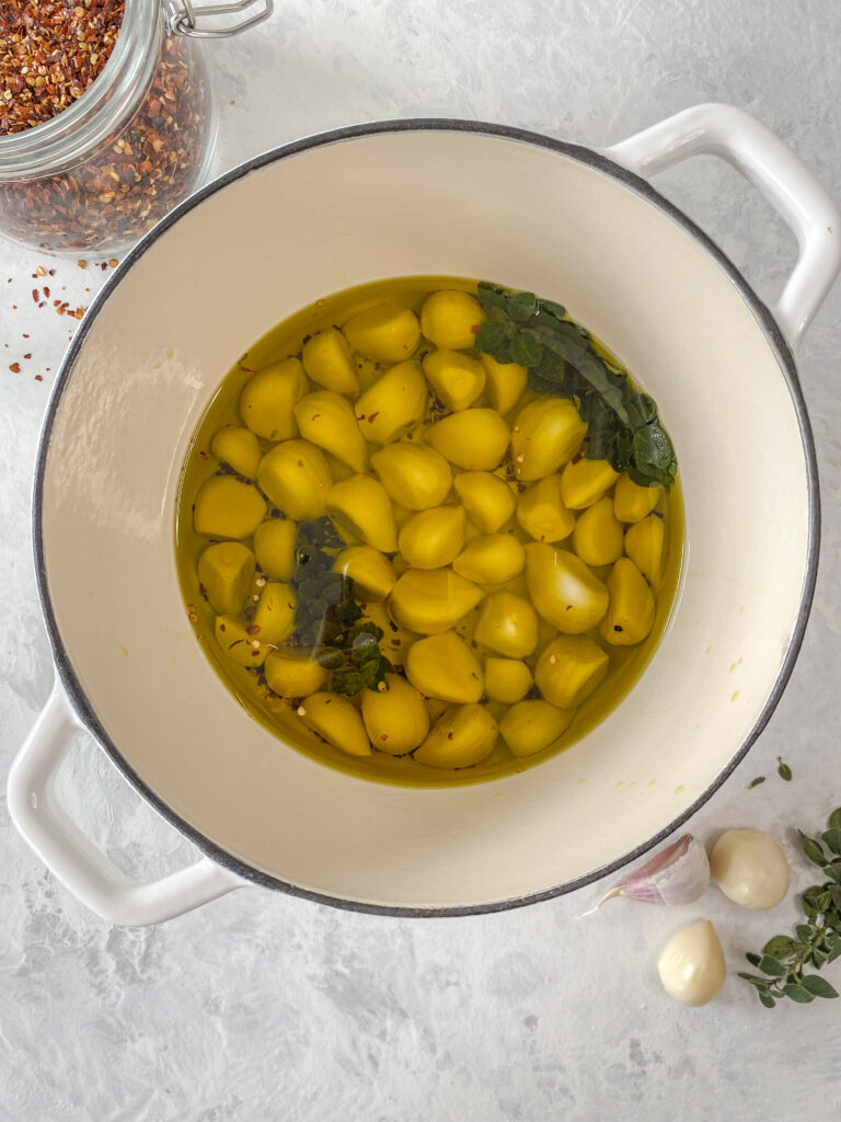 Garlic covered in oil in a white cast-iron pot.