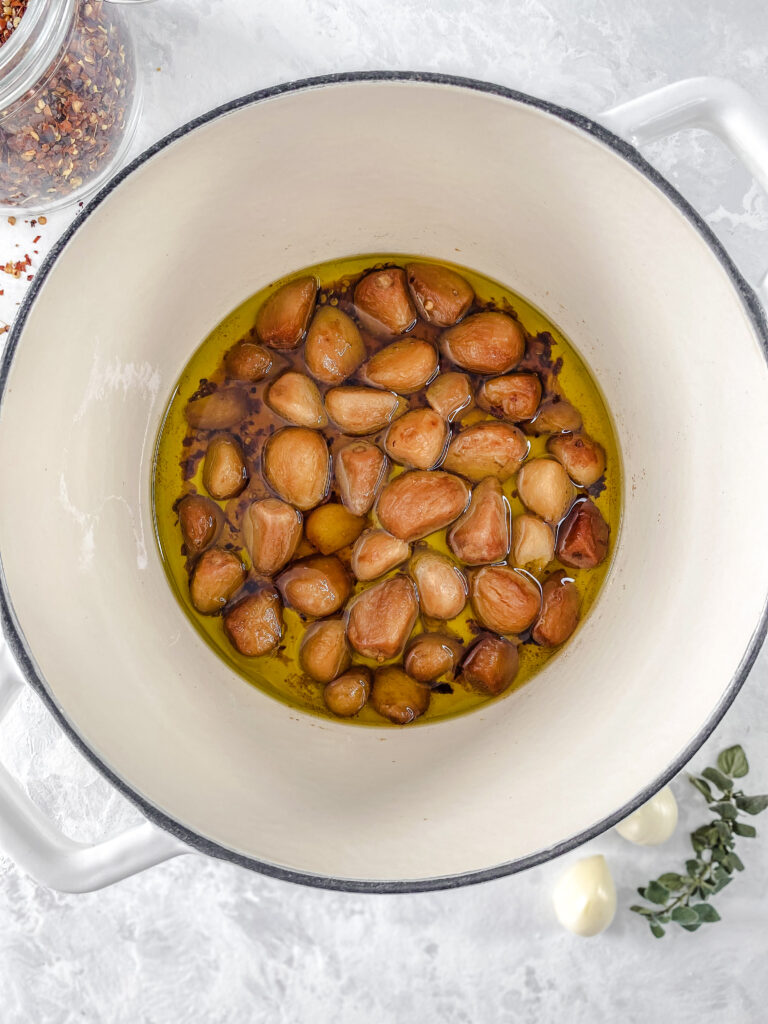 Oven-roasted garlic confit in a white cast-iron pot.