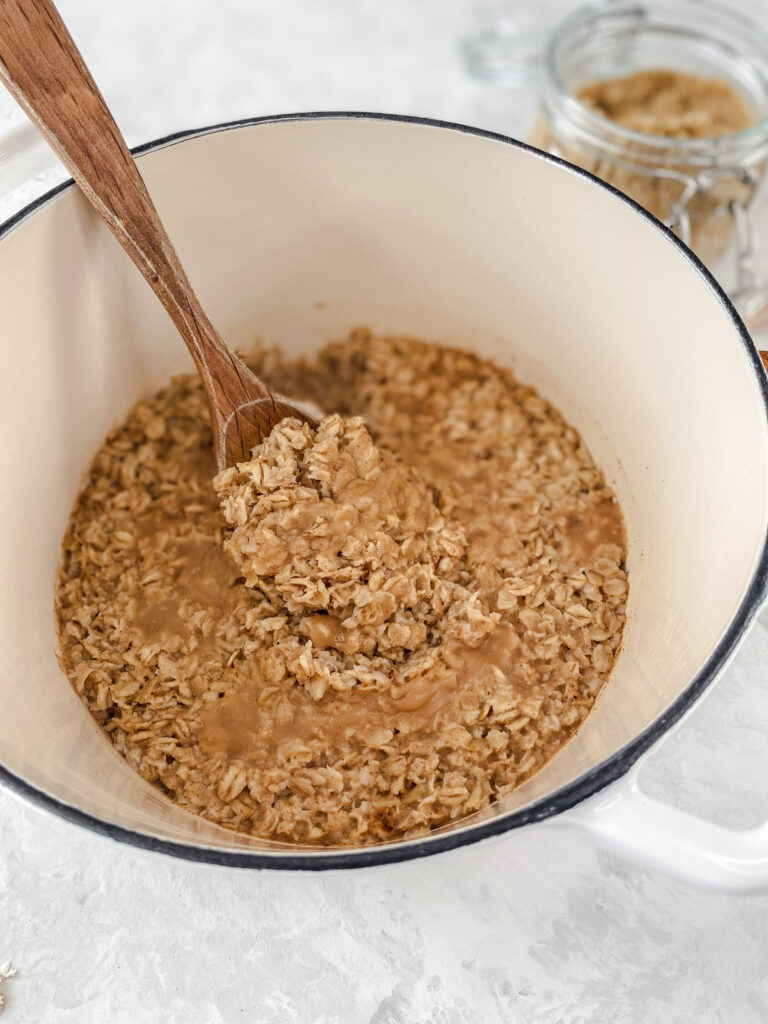 Apple cinnamon oatmeal in a white pot with a wooden spoon.