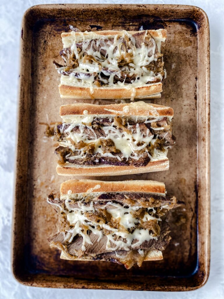 Three French dip sandwiches on a baking sheet.