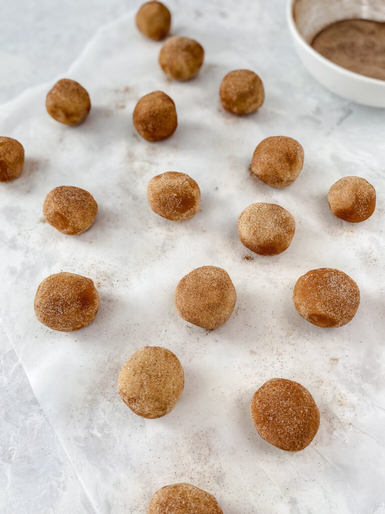 Snickerdoodle cookie dough balls rolled in cinnamon sugar sitting on a marble counter.