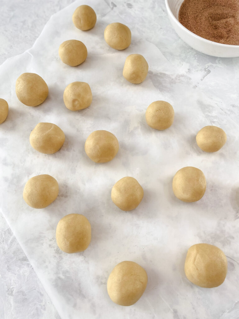 Snickerdoodle cookie dough balls sitting on a marble counter.