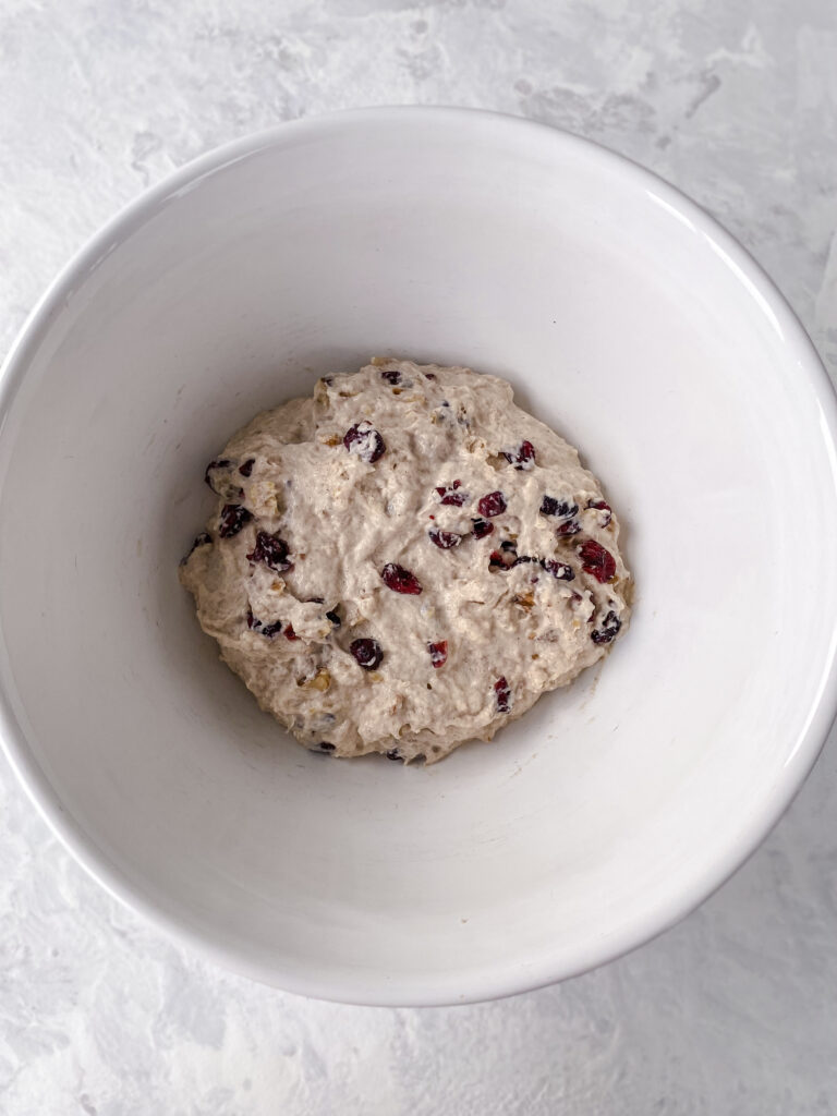 No-knead bread dough with dried cranberries and nuts in a large white bowl.