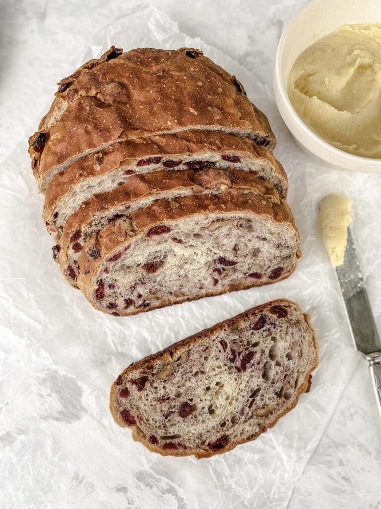 Slices of cranberry walnut bread next to a bowl of honey butter.