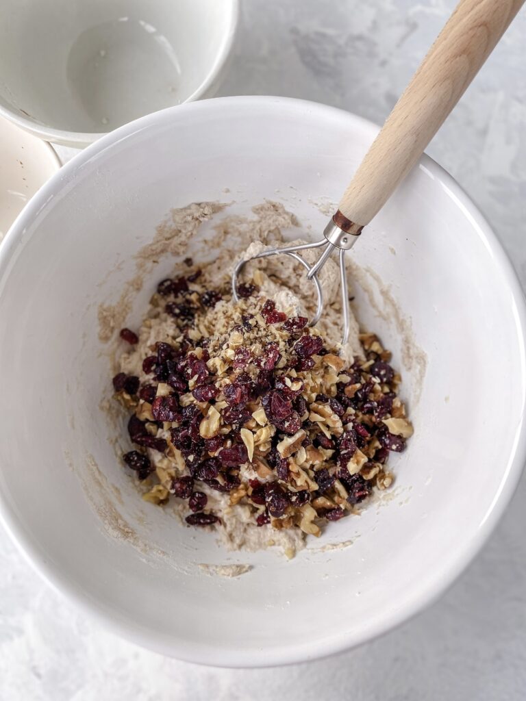 Dried cranberries and walnuts added to a bowl of no-knead bread dough.