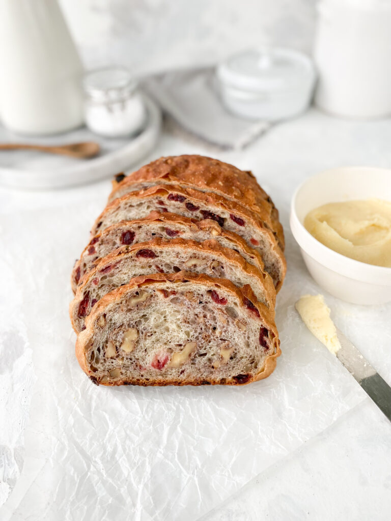 Homemade cranberry walnut bread, sliced next to a knife with butter.