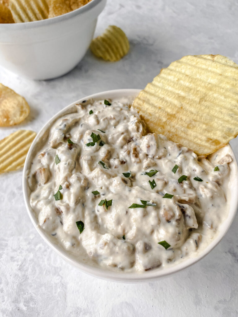 A bowl of French onion dip in front of a bowl of chips.