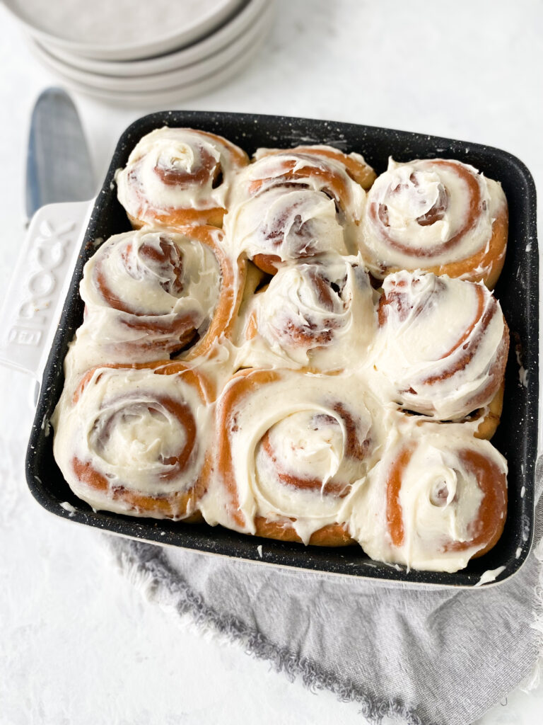 A pan of cinnamon buns topped with cream cheese frosting.