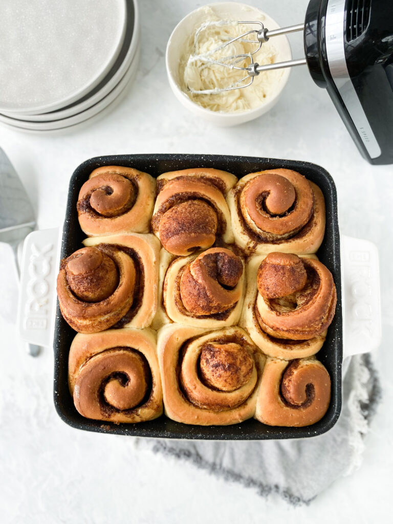 A pan of cinnamon buns beside a bowl of cream cheese frosting.