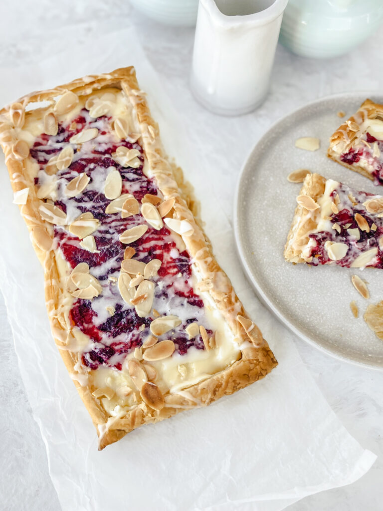 Shareable Puff Pastry Danish filled with sweet cream cheese and homemade cranberry jam, glazed with almond icing, and topped with toasted almonds.