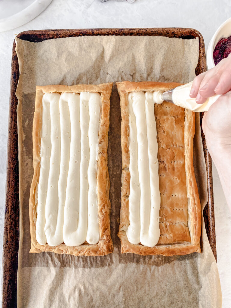 Cream cheese filling being piped into puff pastry tart shells.