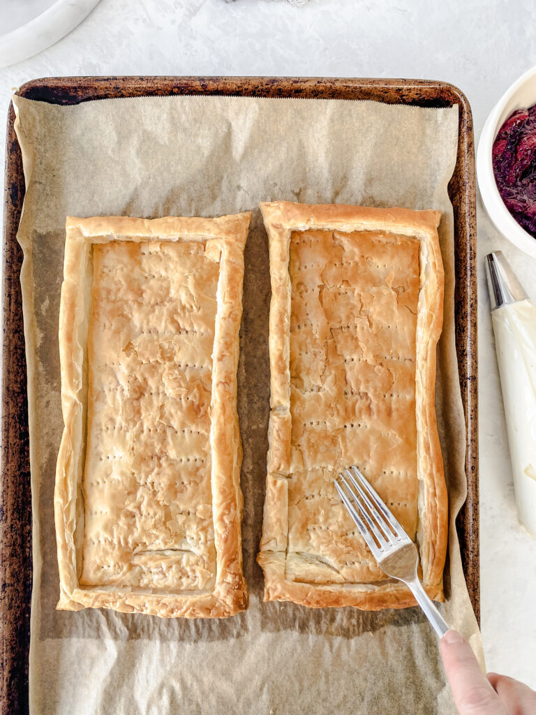 Two rectangles of baked puff pastry being formed into tart shells with the back of a fork.