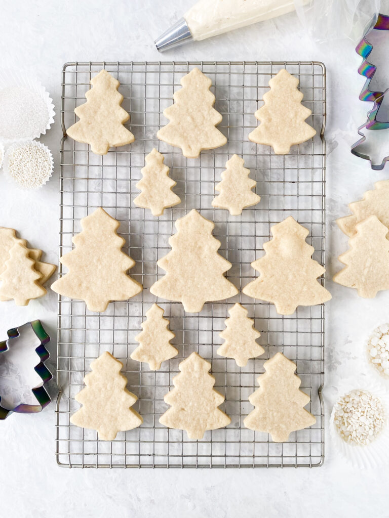 Cut out sugar cookie trees cooling on a wire rack.