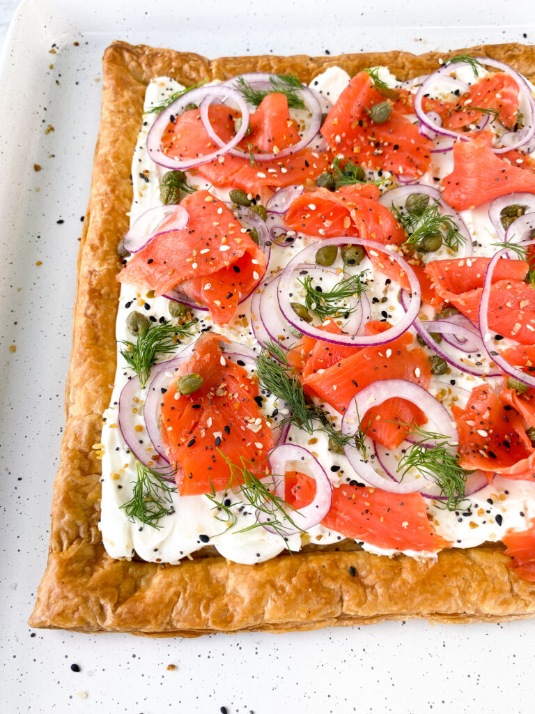 Puff pastry tart topped with whipped cream cheese, smoked salmon, red onion, dill, capers, and everything bagel seasoning.