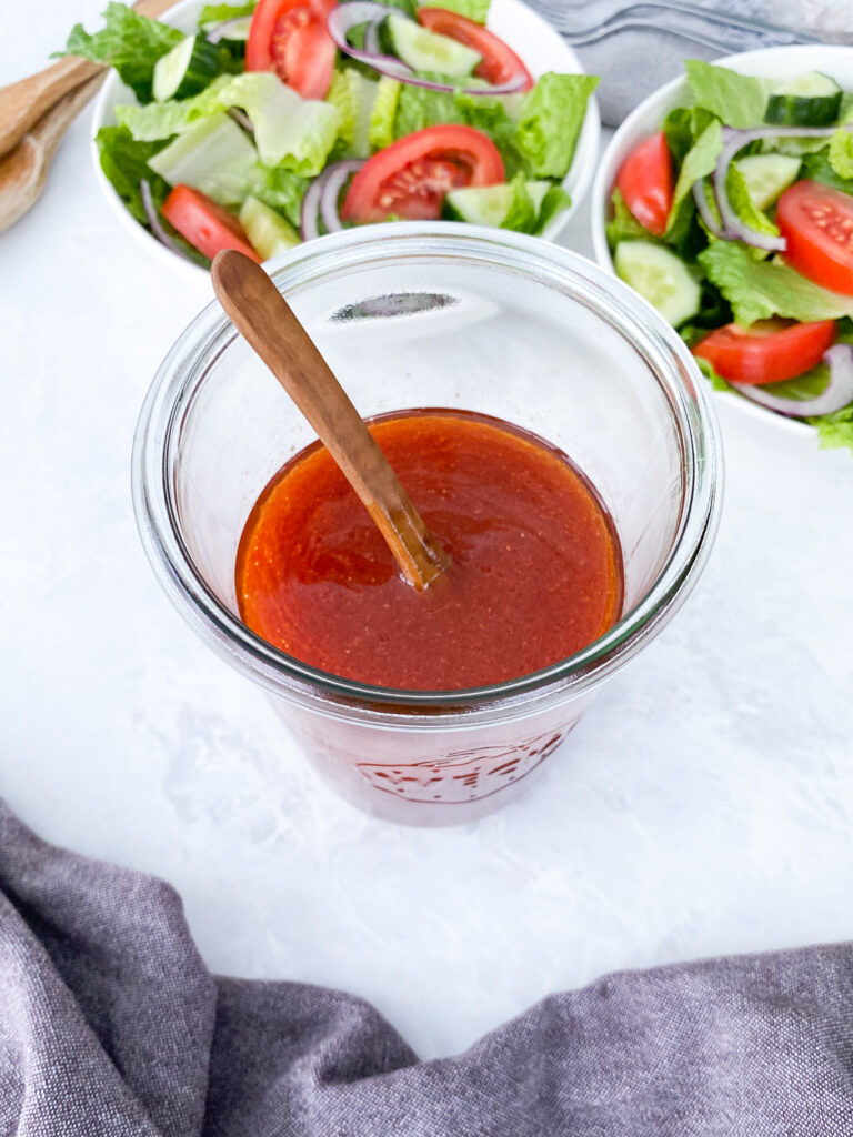 A jar of homemade Catalina salad dressing with two bowls of garden salad.