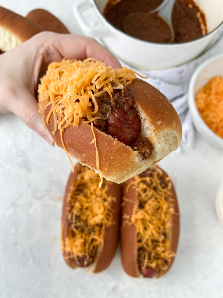 A hand holding a Cincinnati chili dog.