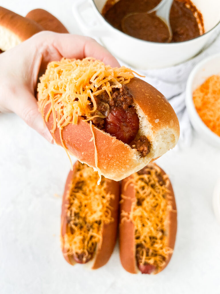 A hand holding a Cincinnati chili dog.