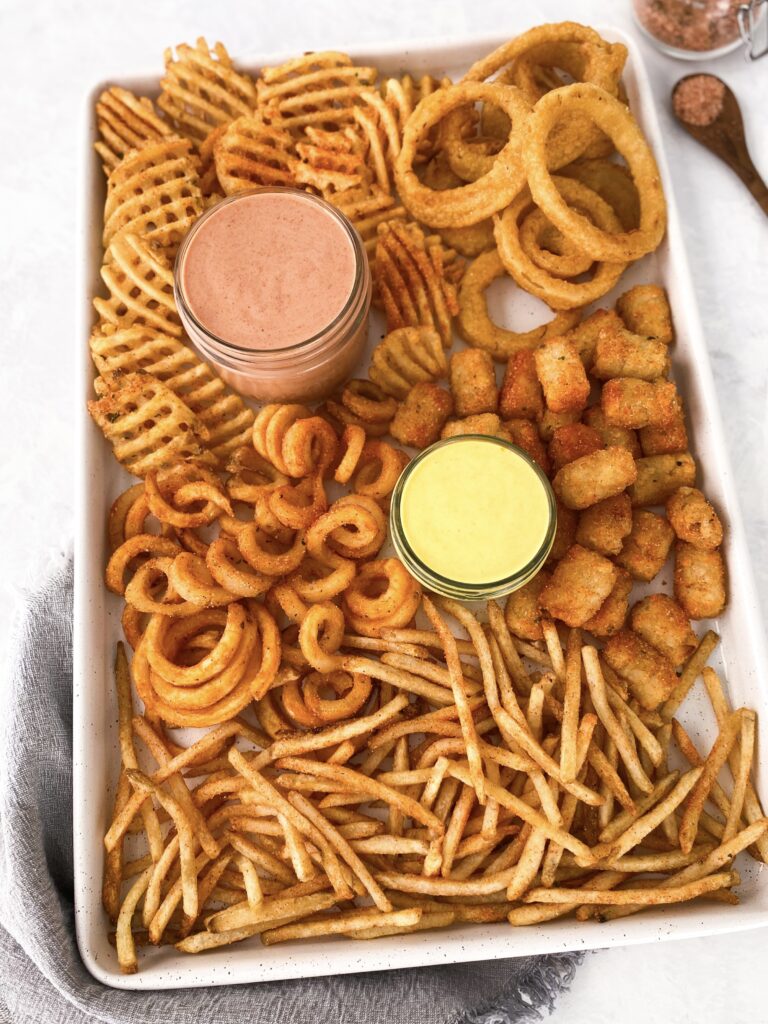 French fry board with onion rings, waffle fries, tater tots, curly fries, and shoestring fries alongside two dips.