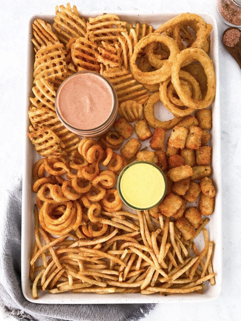 French fry snack board with onion rings, waffle fries, tater tots, curly fries, and shoestring fries alongside two dips.