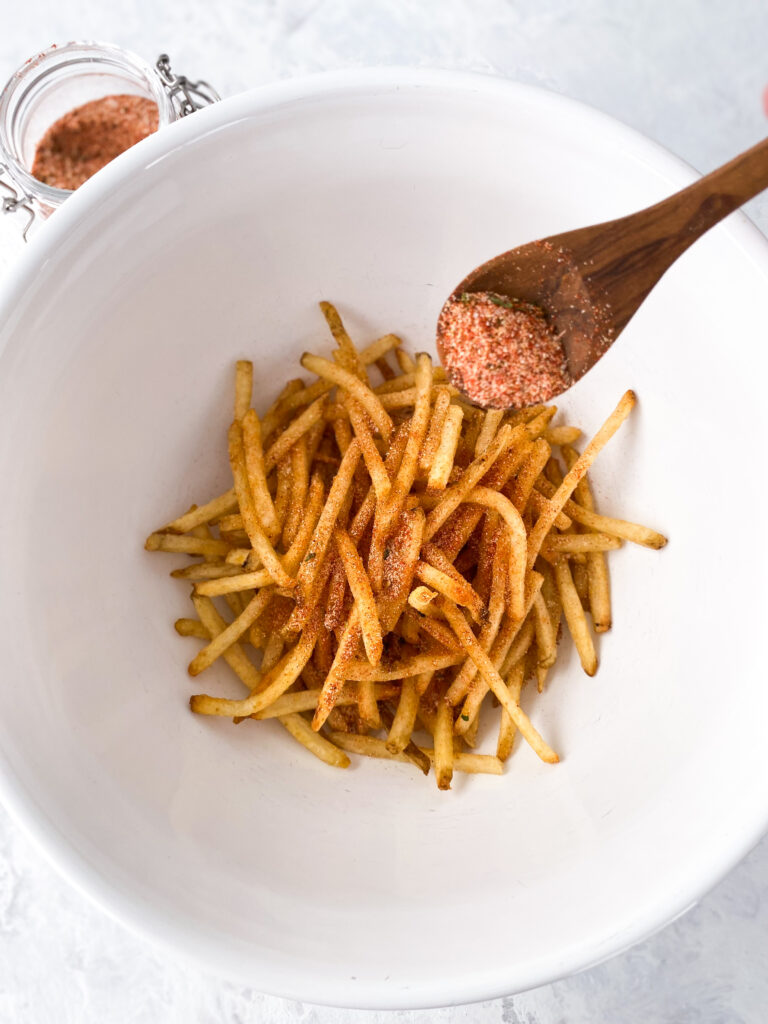 Fry seasoning blend being sprinkled over french fries.