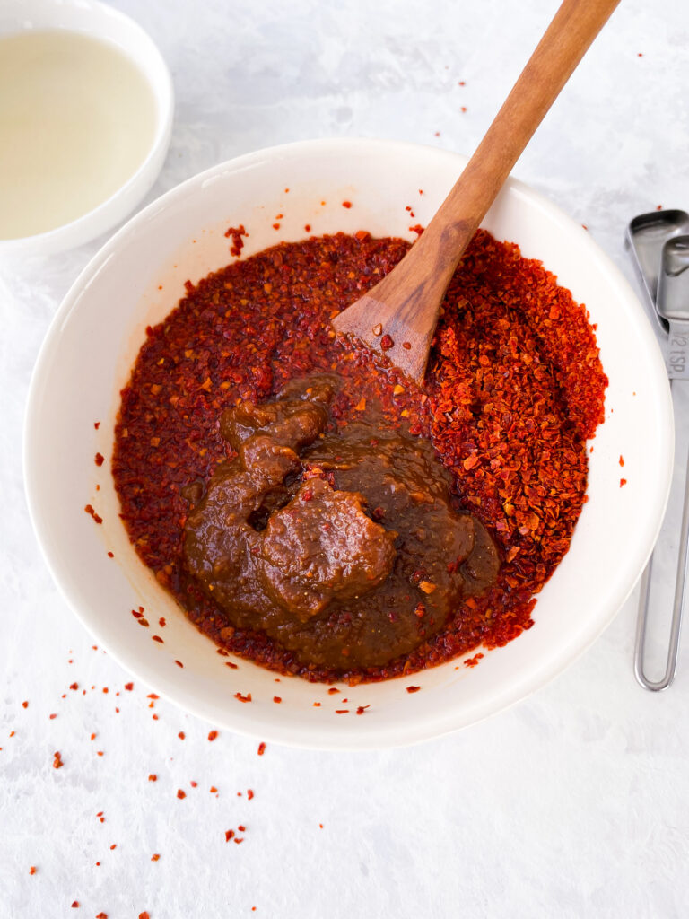 Gochugaru and brown miso paste being stirred together to make gochujang.