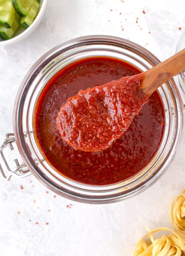 Homemade gochujang being scooped out of a glass jar with a wooden spoon.