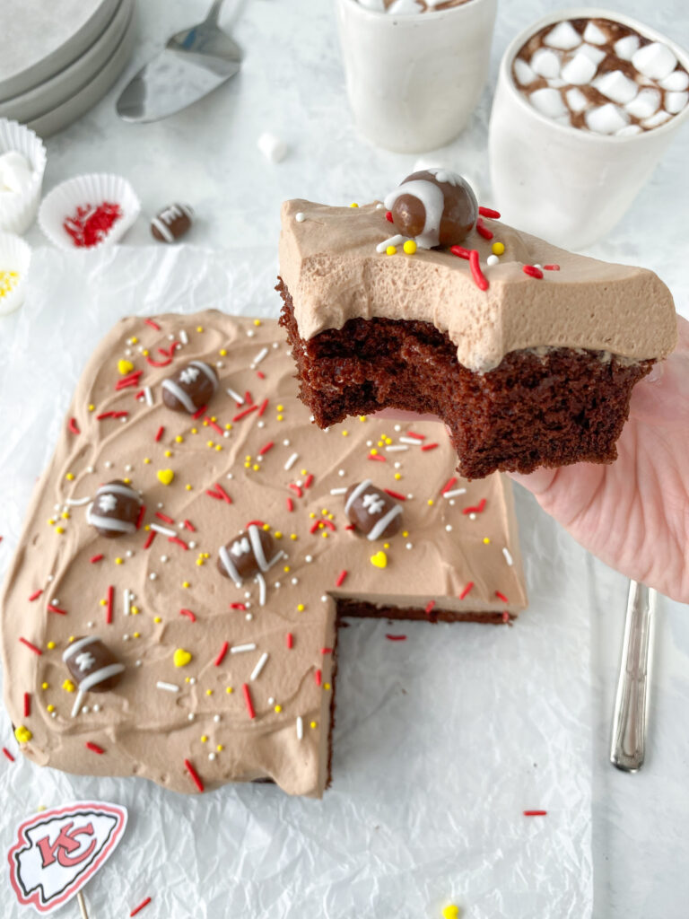 A bitten piece of chocolate mousse cake topped with a chocolate-covered almond football and sprinkles.