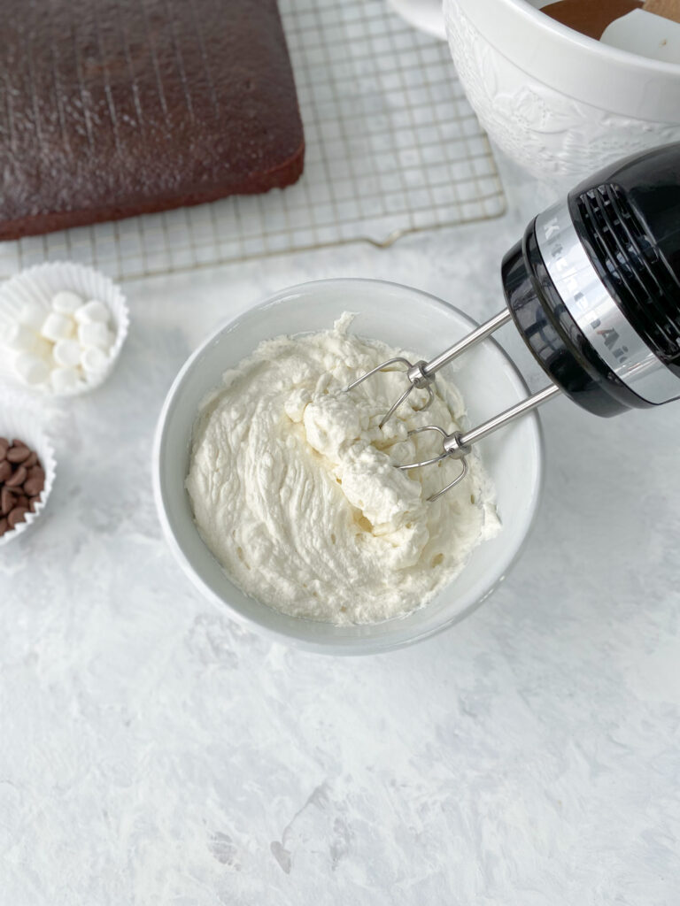 Whipped cream being mixed with a handheld mixer.