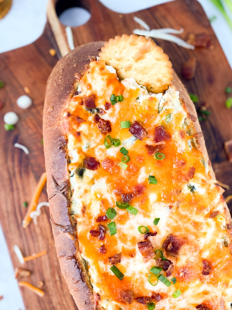 A cracker dipping into Jalapeño Popper Dip stuffed French bread.