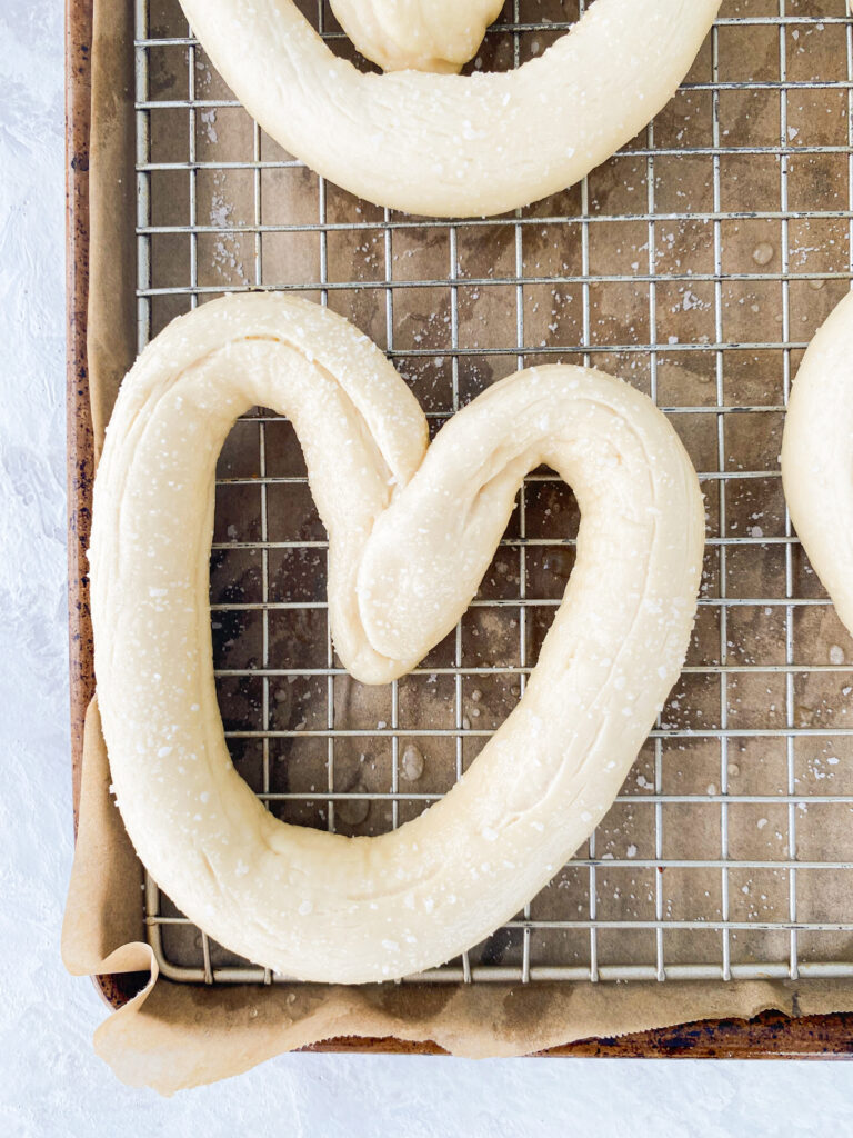 Pretzel dough shaped into hearts, boiled, and sprinkled with salt on a wire rack.