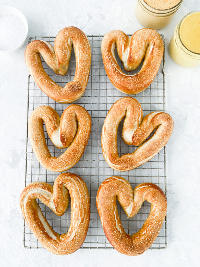 Heart shaped homemade soft pretzels on a wire rack with hot and honey mustard dips.