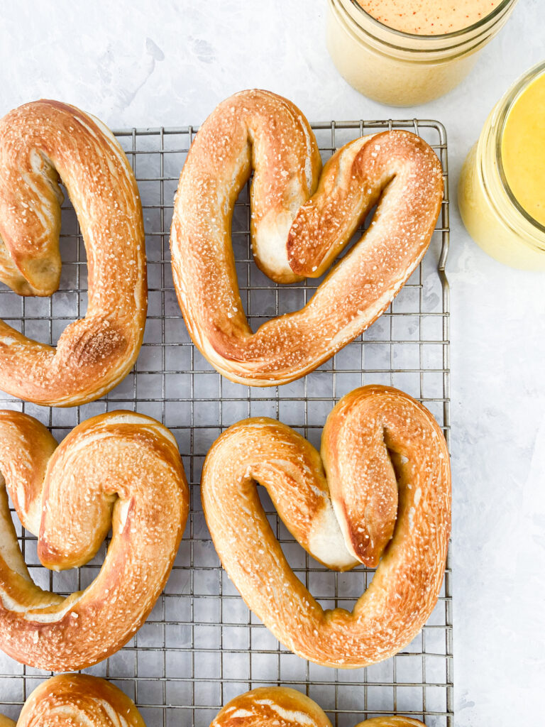 Heart shaped homemade soft pretzels on a wire rack with hot and honey mustard dips.