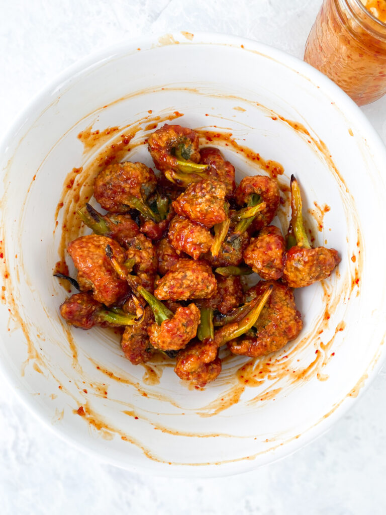 Panko-breaded broccoli tossed with gochujang BBQ sauce in a large white bowl.