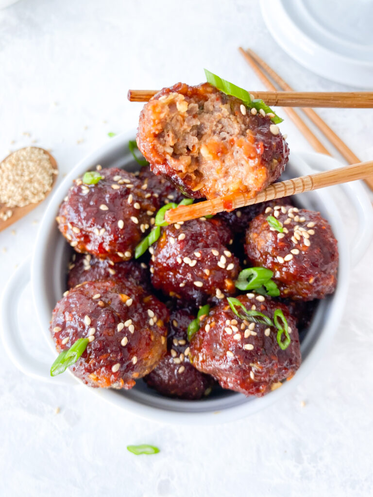 Chopsticks holding a beef meatball glazed in sweet and spicy gochujang sauce.