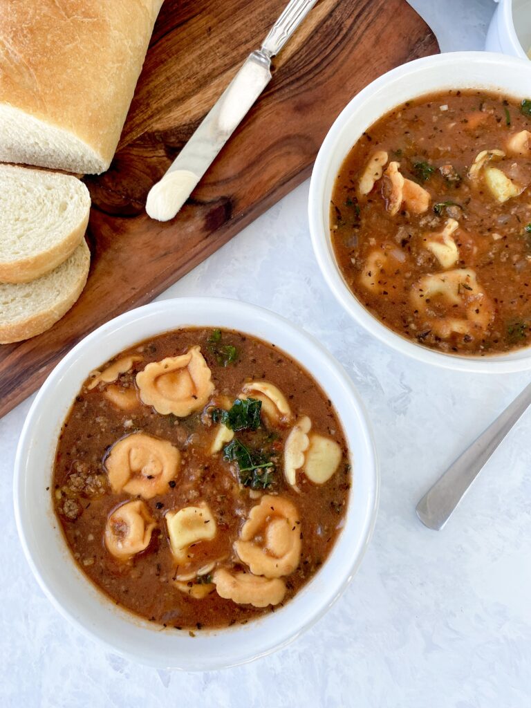 Two bowls of slow cooker tortellini soup with kale and ground beef.