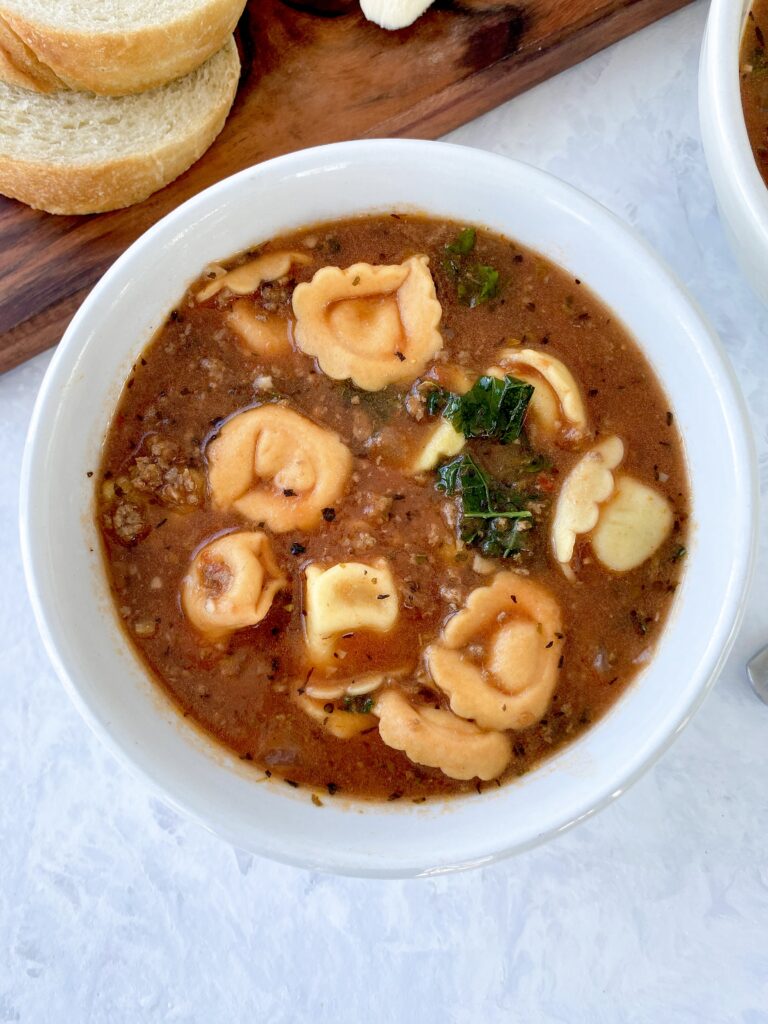 A bowl of tortellini soup with kale and ground beef.