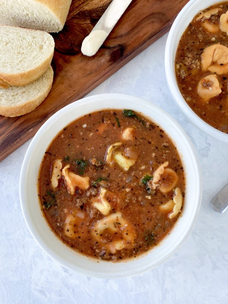 A bowl of tortellini soup with kale and ground beef.