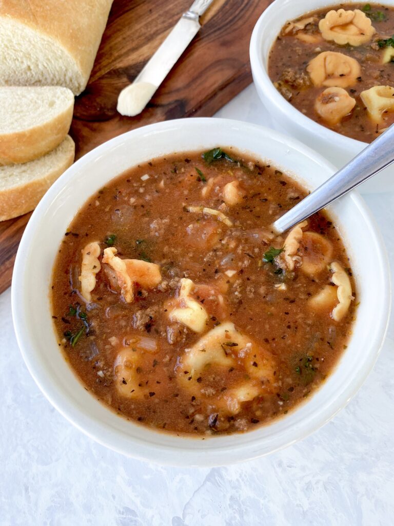 A bowl of tortellini soup with kale and ground beef.