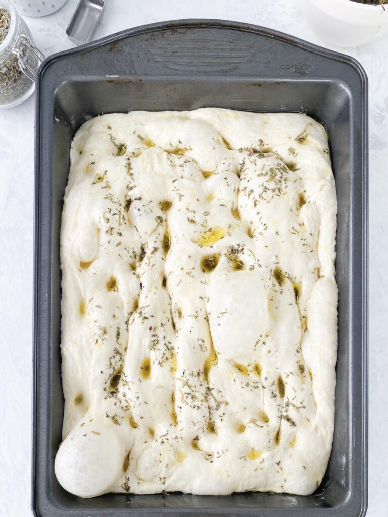 Focaccia dough drizzled with herb oil and dimpled