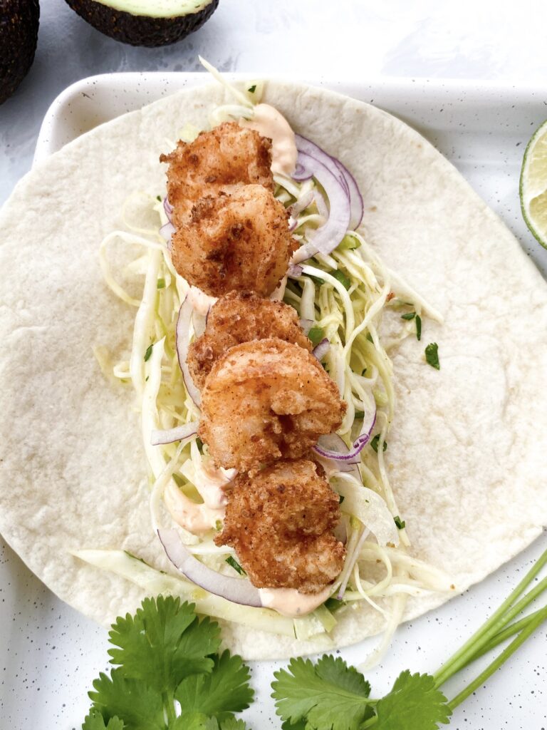 Baja taco filled with crispy jumbo shrimp, crunchy cabbage slaw, thinly sliced red onions, and Baja sauce.
