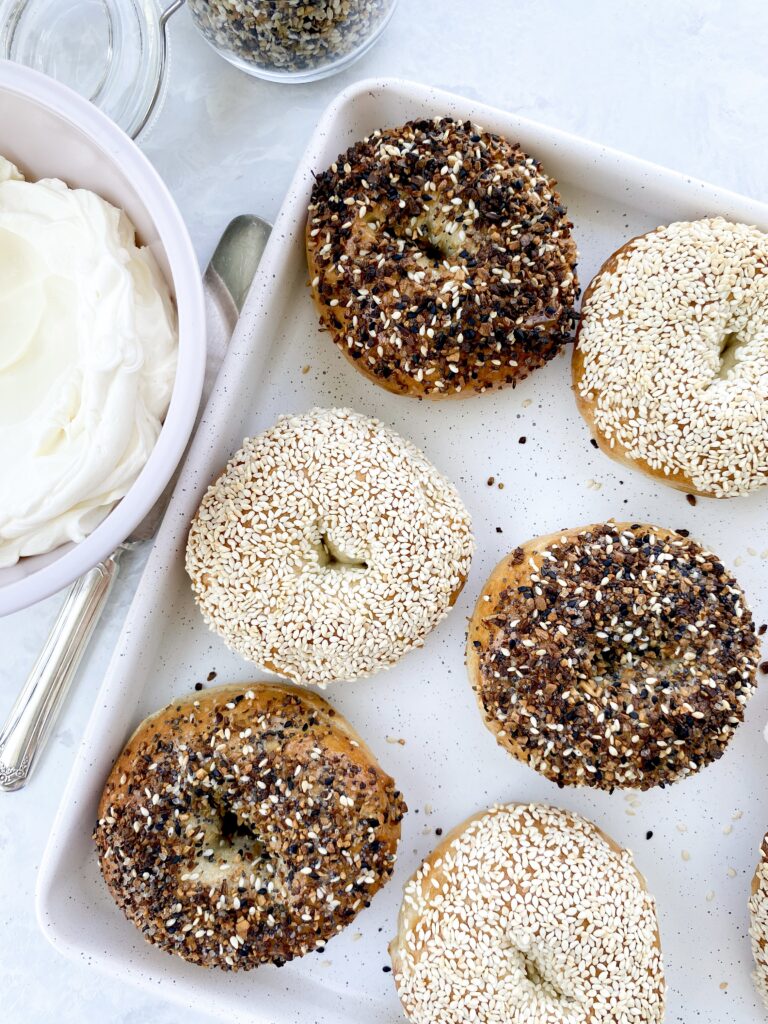 Homemade bagels topped with everything bagel seasoning and sesame seeds on a baking sheet.