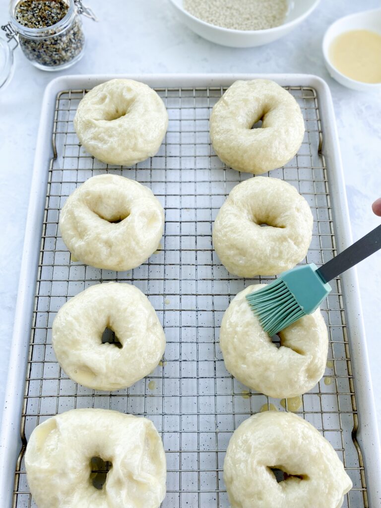 Homemade bagels being brushed with egg wash before baking.