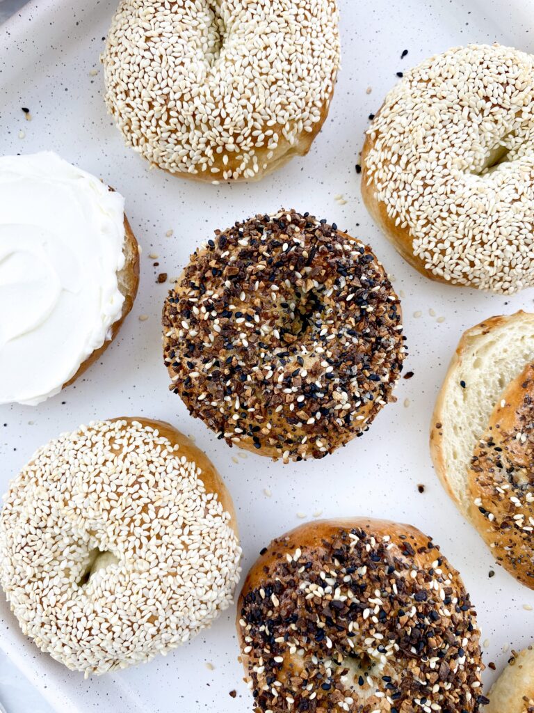 Homemade bagels topped with everything bagel seasoning and sesame seeds with whipped cream cheese.