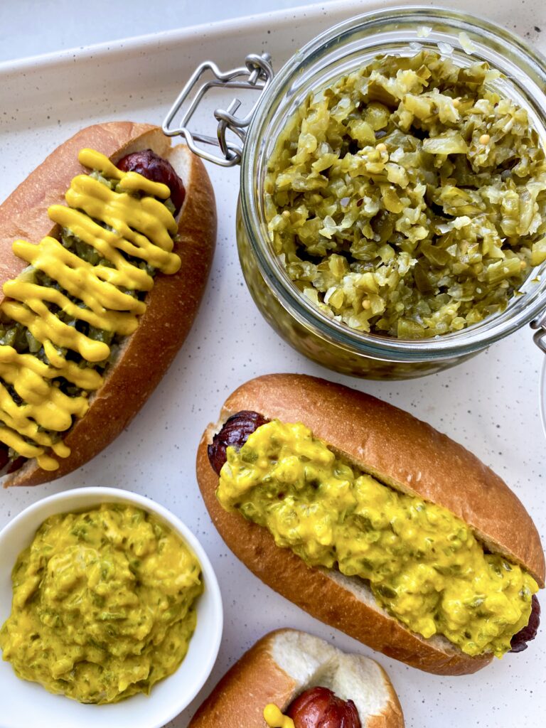 Homemade pickle relish beside dressed hot dogs