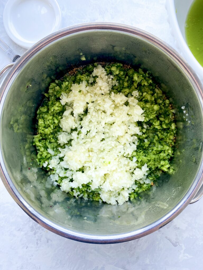 Cucumber and onion added to a pot with pickle brine.
