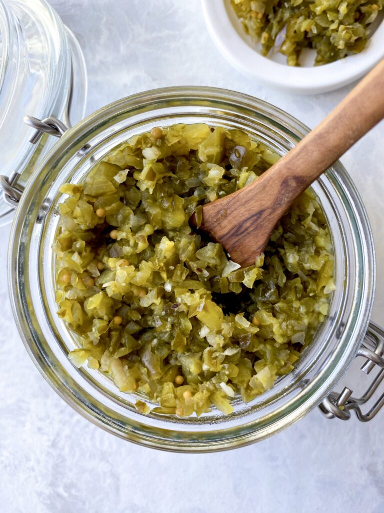 Homemade pickle relish in a glass flip-lid jar with a wooden spoon.